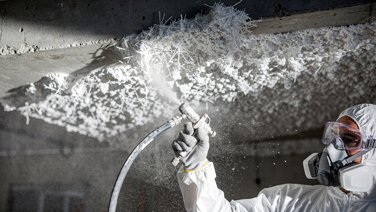 Technician spraying fiberglass acoustic coating on concrete ceiling
